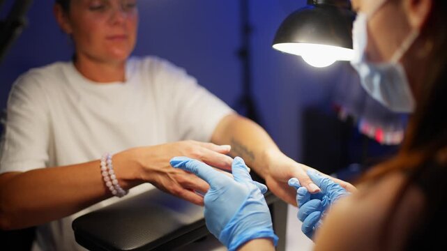 A manicurist is smoothing out the shape of the nail on the client's two thumbs. High quality 4k footage