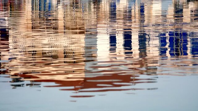 Abstract reflection of the port at sunrise in Elafonisos, Greece&mdash;boats and harbor structures mirrored on rippling water, creating warm golden and blue patterns in calm morning light.