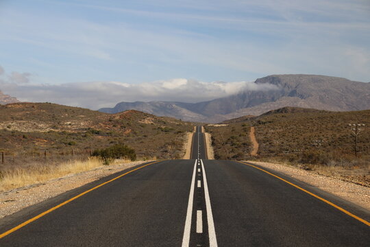 Straight road through arid mountain landscape under partly cloudy sky visioned in a mirror
