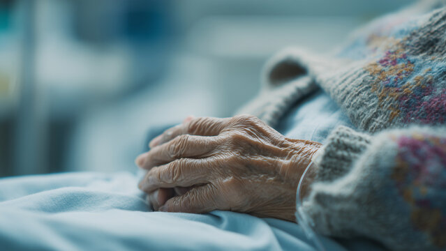 Close-up of a senior person's fragile hands resting gently on a light blue sheet in a hospital bed, symbolizing aging, healthcare, and patient care