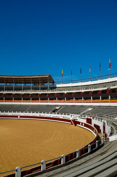 View of the bullring under a vibrant blue sky presents a striking contrast between the ochre sand and concrete seating, Dax, France.