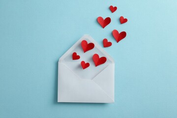 White envelope with red paper hearts flying out on light blue background