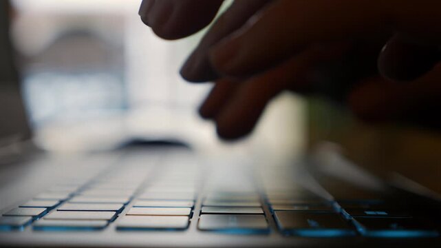 Hands actively type on a laptop keyboard in a cafe as a woman completes work tasks, showing efficiency within a relaxed everyday environment. Focused productivity.