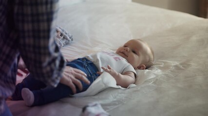 Professional babysitter putting jeans on adorable infant, childcare routine