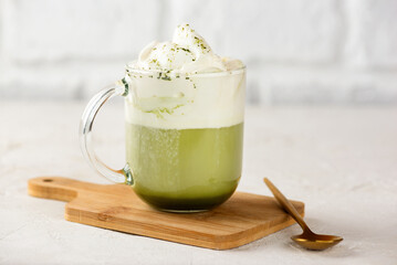 Green tea matcha latte with whipped coconut milk and pistachio with golden spoon on wooden board.