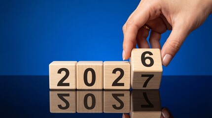 A hand carefully places a wooden block with the number six on top of blocks displaying 2027 symbolizing transition and future planning