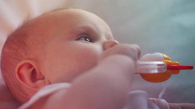 Cute newborn baby playing with teether, exploring textures and sensations