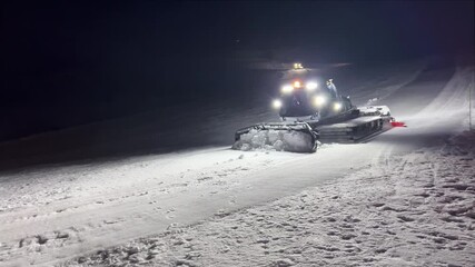 At night, snowcat descends the ski slope, leveling and compacting the snow
