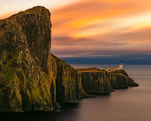 Vertical view of Neist Point lighthouse on dramatic sea cliffs at sunset, Isle of Skye, Scotland, long exposure ocean and colorful sky, iconic coastal travel landscape.