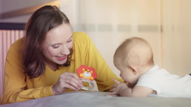 Smiling woman playing with newborn baby girl using colorful teether toy