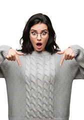 medium close-up of a young caucasian woman with dark wavy hair, round glasses, and textured gray cable-knit sweater, pointing down in urgent shock against a transparent studio background. Urgent