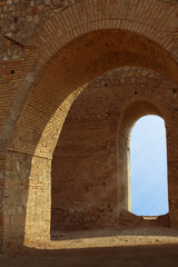 Fototapeta premium Interior view of the historic Bahram Fire Temple in Shahr-e Ray, showing layered arches, textured walls lit by natural light, and a clear blue sky visible through the distant opening.