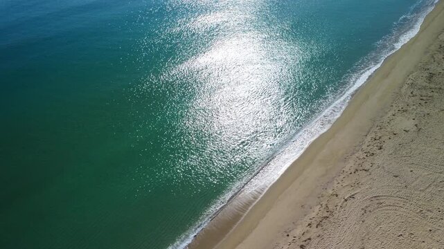 Aerial drone view of Sibari beach with ocean waves and sun shimmering on water, Italy