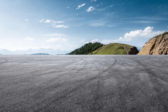 Empty asphalt road and green mountain scenery under blue sky.