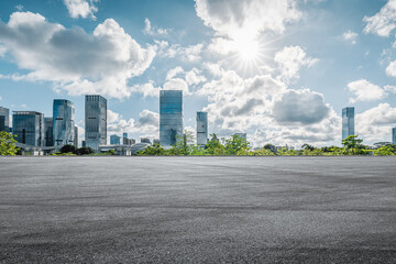 Empty asphalt road and modern city skyline with skyscrapers under a bright sunny sky.