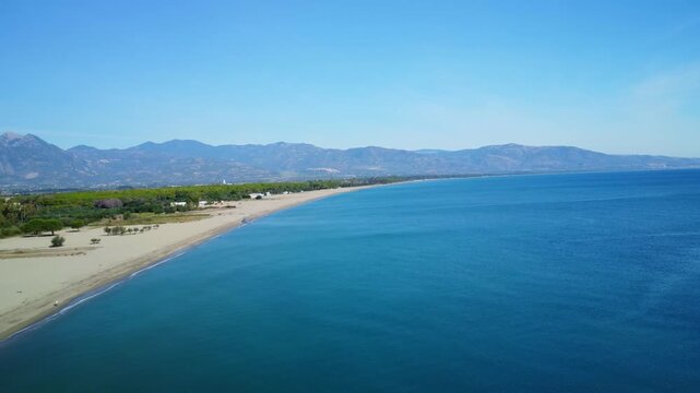 Aerial drone flying right and upward along the coast at Sibari beach Italy with ocean, beach, and mountains in the background