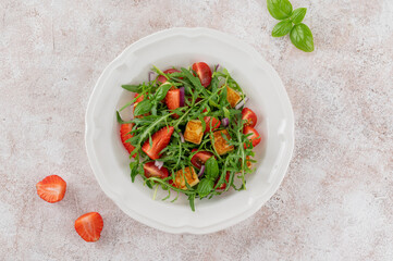 Healthy salad with strawberries, tomatoes, arugula, halloumi cheese and basil on a plate on a concrete background. Top view, copy space.