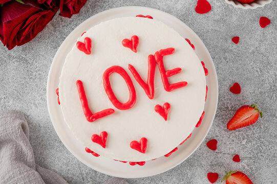 Vanilla strawberry cake with small red hearts for Valentine's day on a white plate on a gray concrete background. Romantic cake.