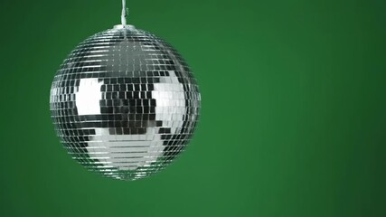 A vibrant, festive silver mirrored disco ball is captured in a clean studio close-up, hanging and reflecting light against a solid emerald green background with ample copy space.