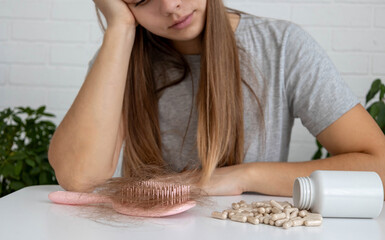 Depressed woman near table with fallen hair on brush and scattered supplement capsules
