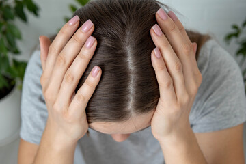 Woman holding her head, showing hair parting and the problem of thinning or hair loss