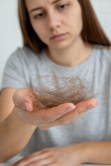 Sad woman holding a bunch of fallen hair in her hand, alopecia and hair loss problem