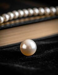 Close up of a single lustrous pearl with a strand of pearls resting on an open book with a velvet background