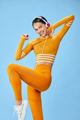 Fitness woman in vibrant orange athletic outfit performs dynamic pose against blue backdrop. Sporty...