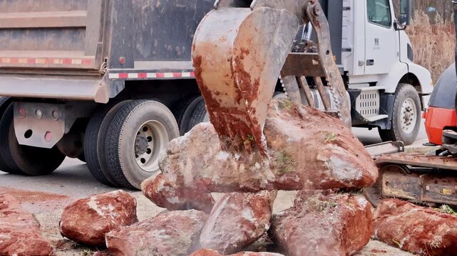 Machine backhoe works to move large rocks at home in suburban neighborhood