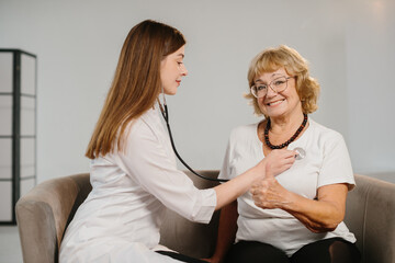 Obraz premium Doctor checking smiling senior woman's heart with stethoscope