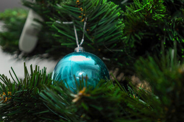 A glossy blue ball hangs gracefully on a silver thread among thick green branches of a Christmas tree. This classic holiday tree with a bright ornament creates a festive mood and a cozy winter atmosph
