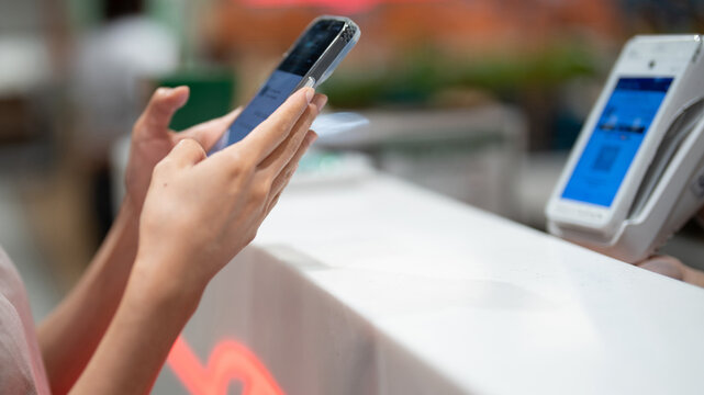 Close up of woman hands using smartphone for contactless scanning QR code or NFC payment at retail store counter.