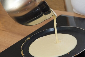 Hobbykoch gie&szlig;t Teig f&uuml;r Palatschinke in Bratpfanne