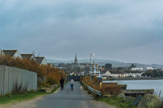 Walkway along the Avoca River leading to Arklow town and church spire on an overcast, muted day.
