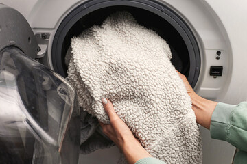 Loading washing machine with soft blanket. Hands putting fleece fabric into washer drum. Home laundry routine indoors. Household cleaning process. Washing clothes at home. Textile care and hygiene. © Paweł Michałowski