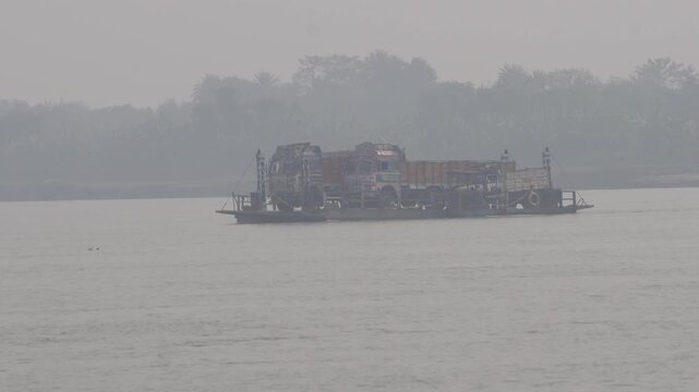 Ferry boat overloaded with trucks crossing foggy Ganga river