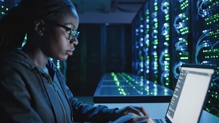 Female IT Engineer Working on Laptop in Data Center. Black woman managing server racks, network infrastructure, and cybersecurity in modern tech fa... - Powered by Adobe