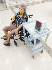 Senior woman sitting in a wheelchair having her blood pressure measured with a digital medical monitor in a hospital. Healthcare and medical concept representing elderly care, patient monitoring, reha
