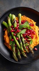 Delicious grilled asparagus served on a bed of creamy sweet potato mash, garnished with vibrant pomegranate seeds and fresh mint leaves, perfect for a healthy meal.