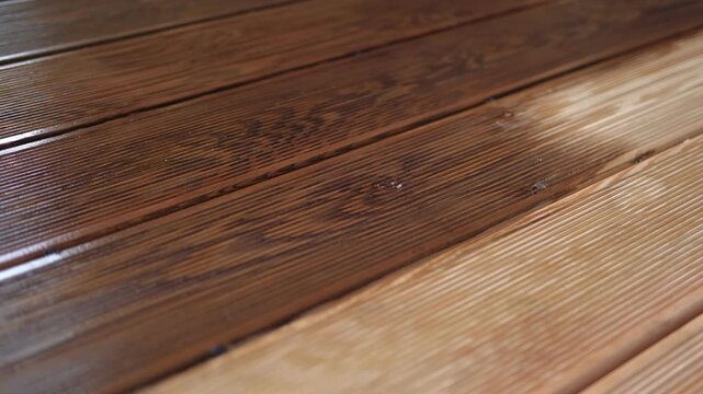 Brown oil for protection of wood by staining. Painting a larch for protecting and pests. Woodworker applying finish to terrace deck board. Repairman varnishing with brush wooden plank floor surface.