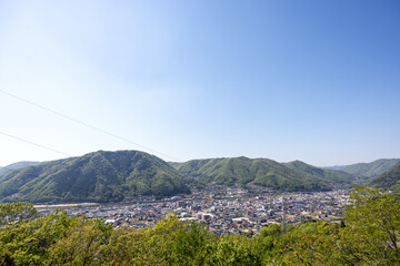 青空の下に広がる緑の山々に囲まれた地方都市の遠景