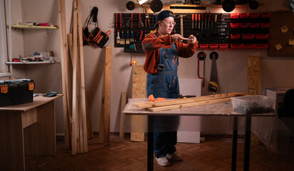 professional female carpenter works with wood using carpentry tools in her garage. She stands holding a phone and takes photos of the workpieces. Conceptualization of profession, art, and hobby.
