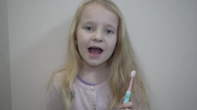 A girl is getting ready to brush her teeth, holding a toothbrush, A little girl with blue eyes is holding a toothbrush