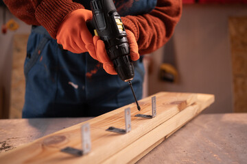 close-up of a man's hand holding a cordless electric screwdriver and screws used for fastening wooden structures. He is fixing a metal corner.