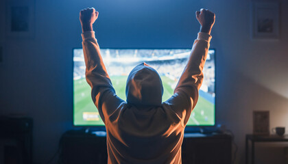 Fan in Hoodie Celebrating Soccer Victory in Front of TV Screen