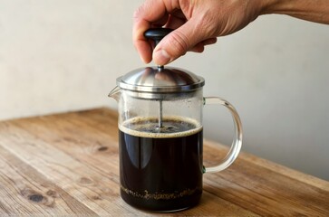 Hand Plunging a French Press Coffee Maker on a Wooden Table
