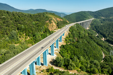Aerial view of a highway viaduct bridge spanning a lush green mountain valley. Modern transportation infrastructure, engineering. Road trip travel