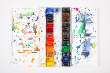 Used watercolor paint palette with colorful paint splatters and stains on white paper, artistic creative mess from painting activity, top view flat lay