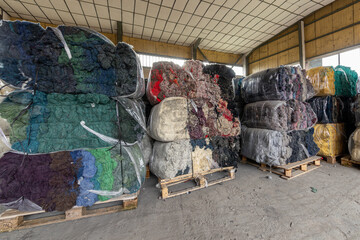 Warehouse with stacked bales of colorful recycled textile fibers. Sustainable raw material for the circular economy and fabric production in a factory.