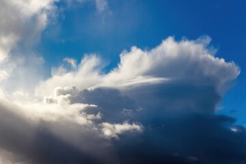 Obraz premium Dramatic dark storm clouds contrasting sharply with bright white illuminated edges and deep blue sky, suggesting dynamic weather conditions or autumn sunset hues